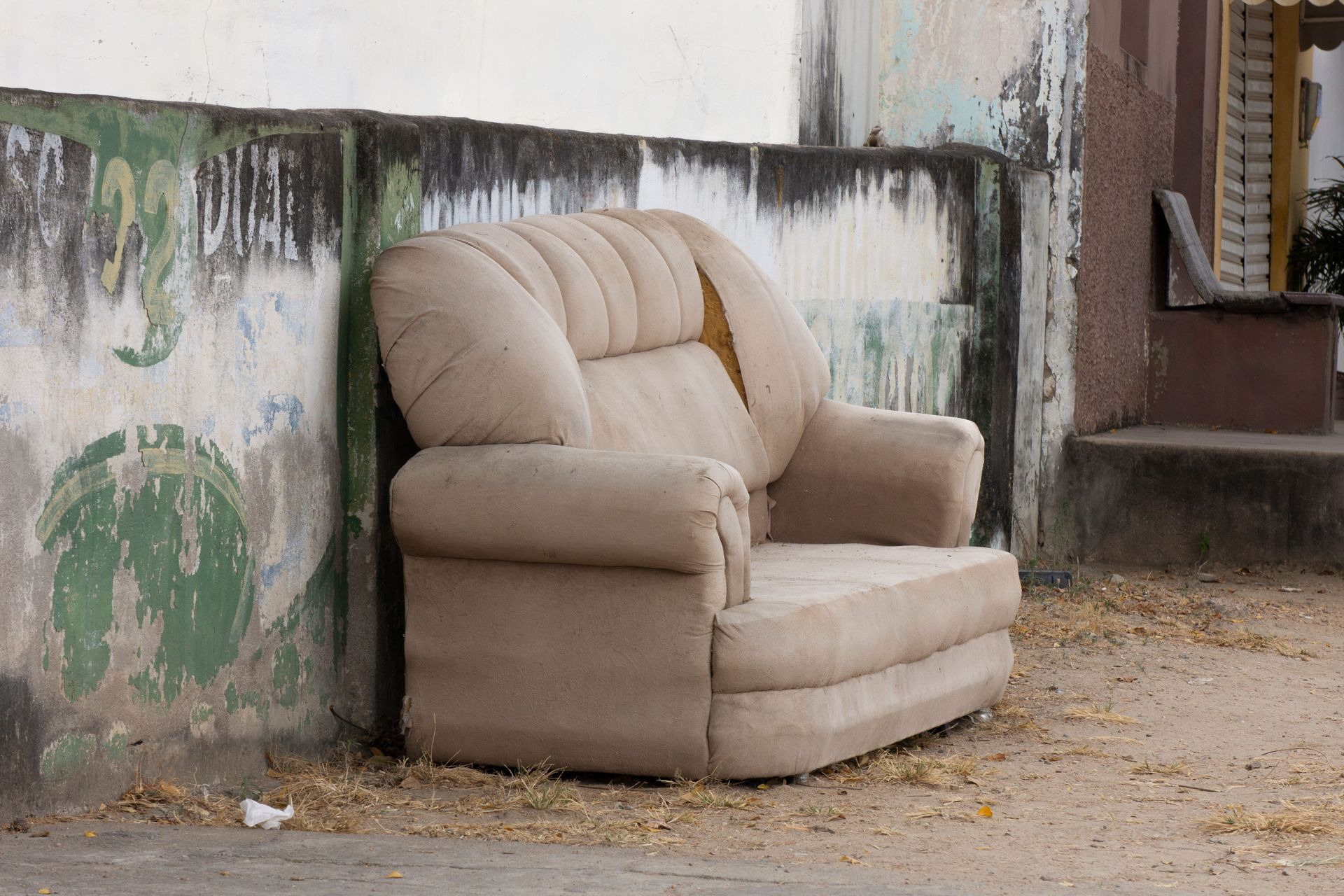 Old beige sofa discarded against a weathered urban wall, symbolizing neglect.