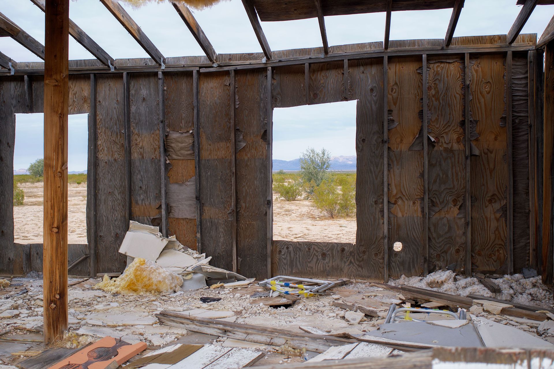Interior view of an abandoned house showing decay and desert landscape outside.